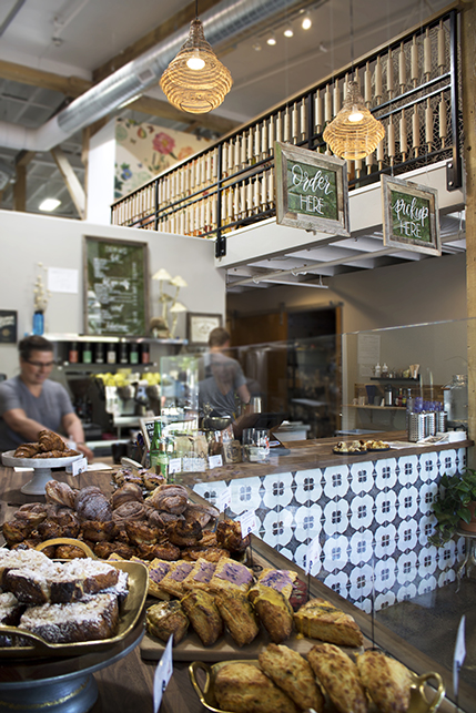 The counter sits in the foreground displaying artisan pastries, the coffee bar, mezzanine, and woven light fixtures can be seen